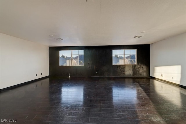 spare room with wood finished floors, visible vents, and baseboards