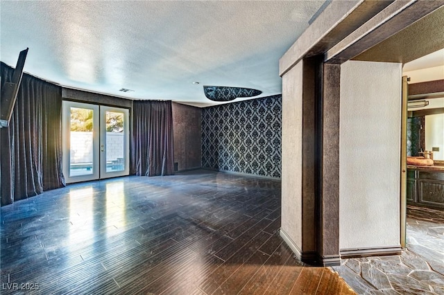 empty room with a textured ceiling, wood finished floors, visible vents, french doors, and wallpapered walls