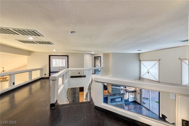 interior space featuring visible vents, a textured ceiling, wood finished floors, and an upstairs landing