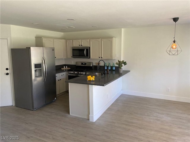 kitchen with light wood finished floors, stainless steel appliances, dark countertops, a sink, and a peninsula