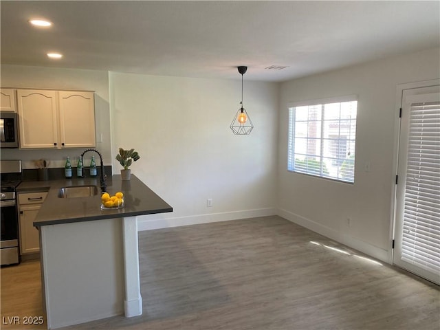 kitchen featuring light wood finished floors, stainless steel appliances, dark countertops, a sink, and a peninsula