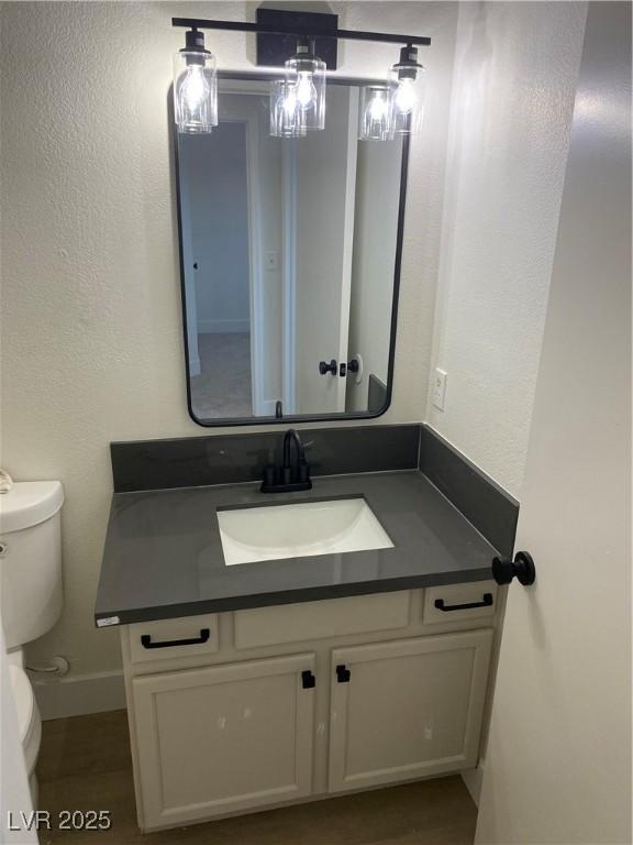 half bathroom featuring a textured wall, vanity, and toilet