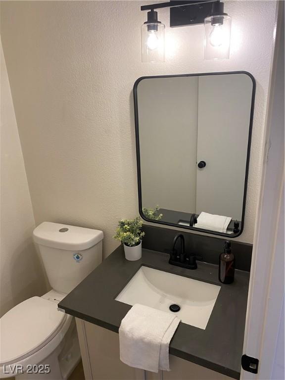 bathroom featuring toilet, a textured wall, and vanity