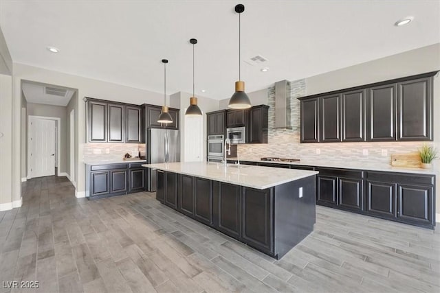 kitchen with stainless steel appliances, a spacious island, visible vents, wall chimney range hood, and decorative light fixtures