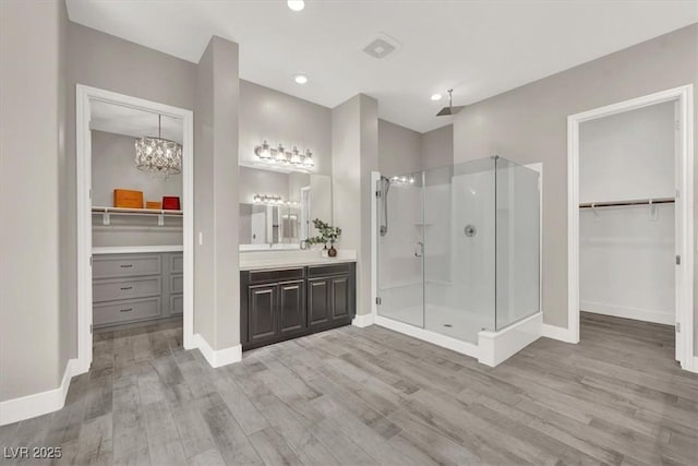 bathroom featuring vanity, wood finished floors, a shower stall, and a walk in closet