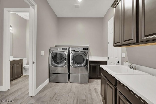 laundry area with washing machine and dryer, a sink, baseboards, light wood-style floors, and cabinet space