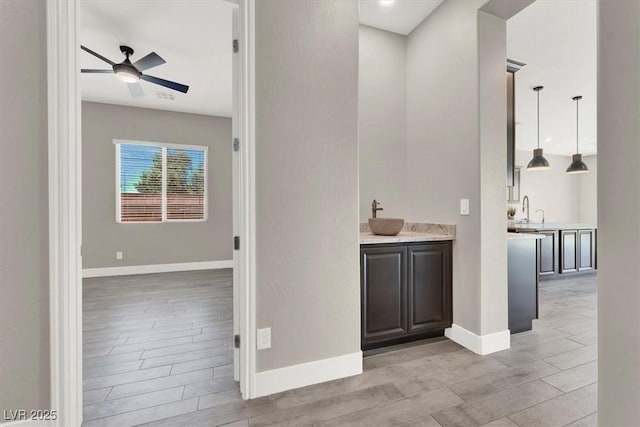 bar featuring wood finish floors, a sink, ceiling fan, and baseboards