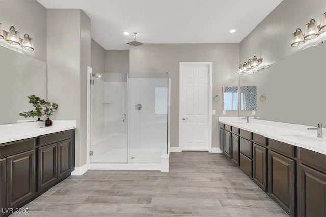 bathroom with wood finished floors, a sink, baseboards, double vanity, and a stall shower