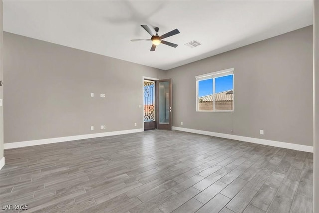 empty room with a ceiling fan, visible vents, baseboards, and wood finished floors