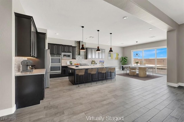 kitchen with a breakfast bar area, stainless steel appliances, light countertops, backsplash, and light wood finished floors