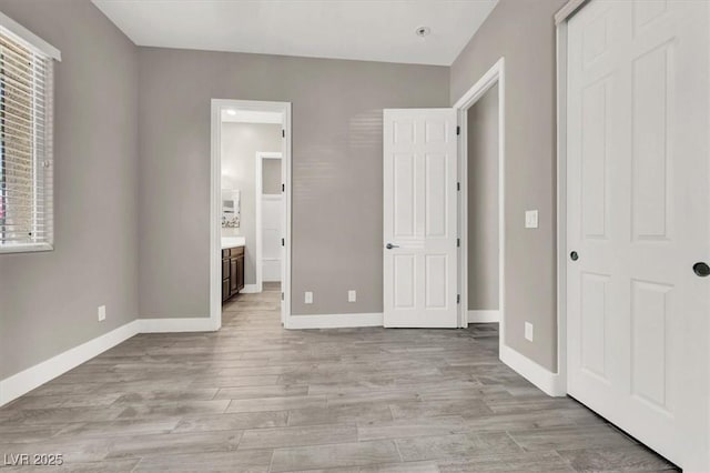 unfurnished bedroom featuring light wood-style floors, baseboards, and ensuite bathroom