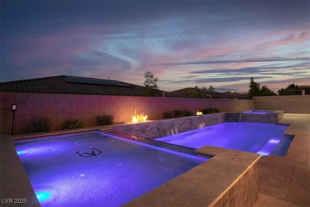 pool at dusk featuring a patio area, a pool with connected hot tub, and a fenced backyard