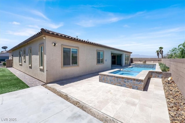 rear view of property featuring a tile roof, a fenced backyard, an in ground hot tub, a patio area, and stucco siding