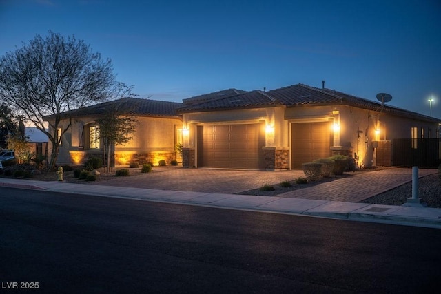 view of front facade featuring a garage, stone siding, a tiled roof, decorative driveway, and stucco siding