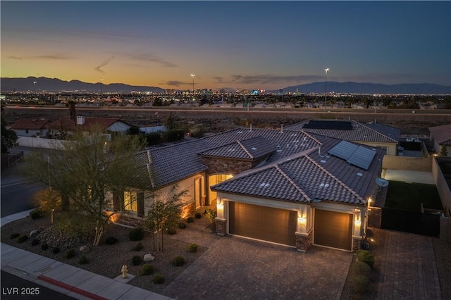 view of front facade featuring decorative driveway, an attached garage, a mountain view, stone siding, and a tiled roof