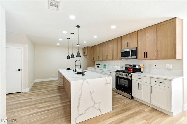 kitchen featuring light stone counters, recessed lighting, appliances with stainless steel finishes, light wood-style floors, and a sink