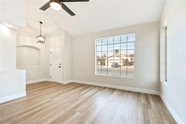 spare room featuring lofted ceiling, baseboards, light wood finished floors, and ceiling fan with notable chandelier