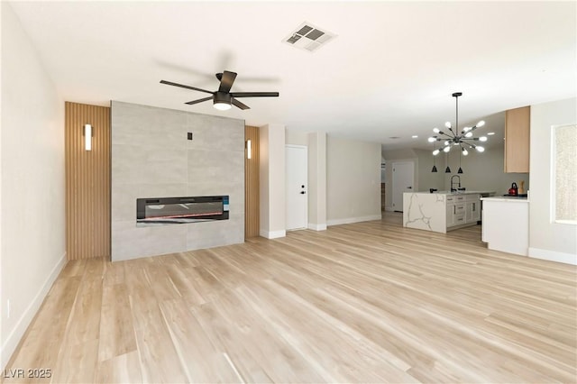 unfurnished living room featuring light wood finished floors, baseboards, visible vents, a tile fireplace, and ceiling fan with notable chandelier