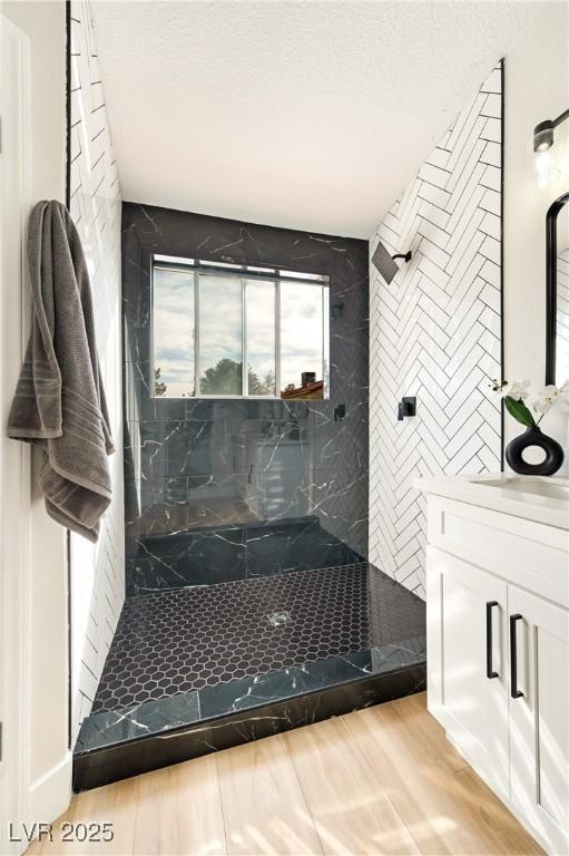 full bathroom with a textured ceiling, tiled shower, and vanity