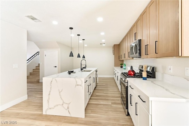 kitchen featuring visible vents, an island with sink, appliances with stainless steel finishes, light wood-style floors, and a sink