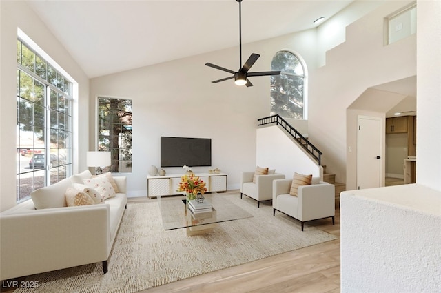 living area with a healthy amount of sunlight, high vaulted ceiling, stairway, and wood finished floors