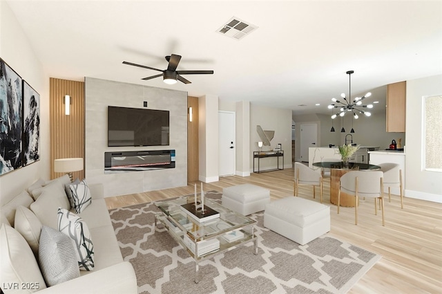 living room with light wood-type flooring, visible vents, baseboards, and ceiling fan with notable chandelier