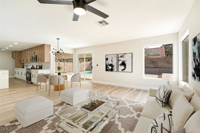 living room with light wood-type flooring, visible vents, baseboards, and ceiling fan with notable chandelier