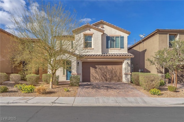 mediterranean / spanish home featuring a garage, decorative driveway, a tiled roof, and stucco siding