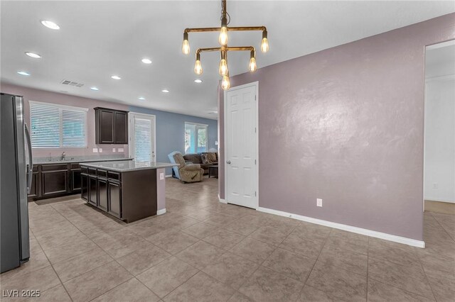 kitchen featuring a sink, open floor plan, light countertops, freestanding refrigerator, and a center island