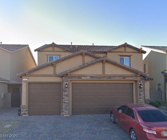 view of front of home featuring stone siding, stucco siding, an attached garage, and decorative driveway