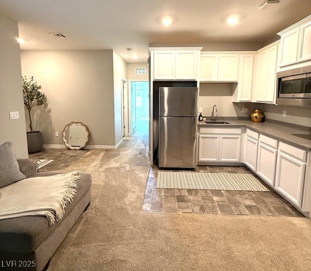 kitchen with a sink, appliances with stainless steel finishes, white cabinetry, dark countertops, and carpet flooring