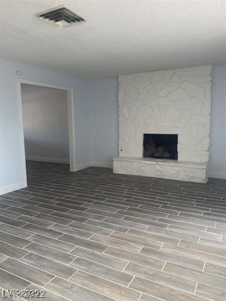 unfurnished living room featuring a textured ceiling, a stone fireplace, visible vents, and wood tiled floor