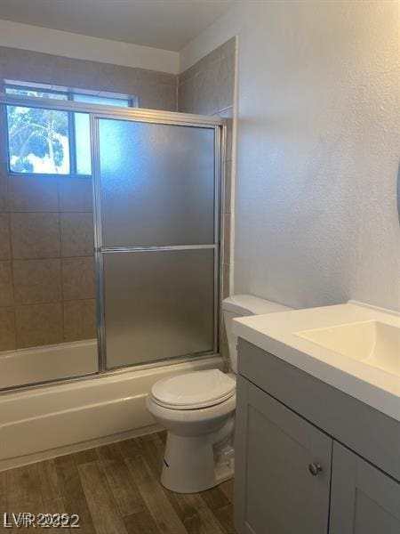 full bath featuring enclosed tub / shower combo, vanity, wood finished floors, and toilet