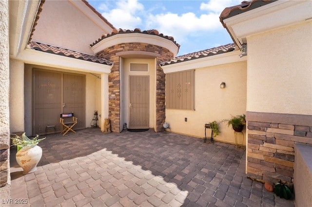 view of exterior entry featuring a tiled roof, a patio area, and stucco siding