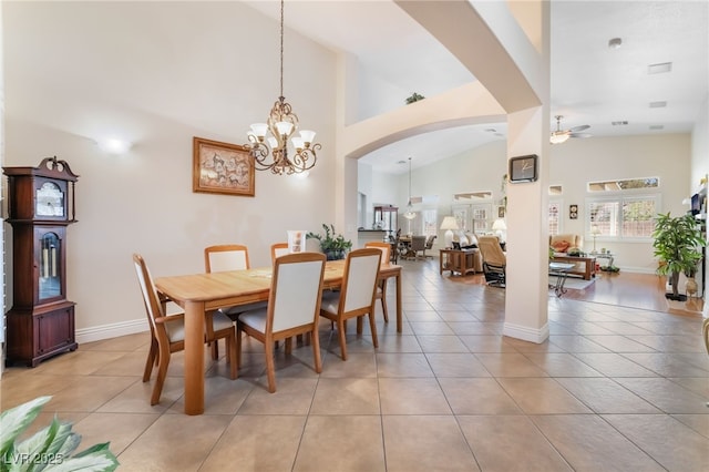 dining space featuring high vaulted ceiling, ceiling fan with notable chandelier, arched walkways, light tile patterned floors, and baseboards