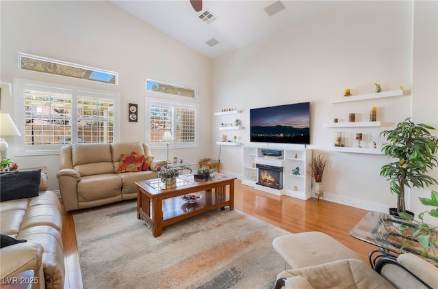 living area featuring wood finished floors, visible vents, a warm lit fireplace, and high vaulted ceiling