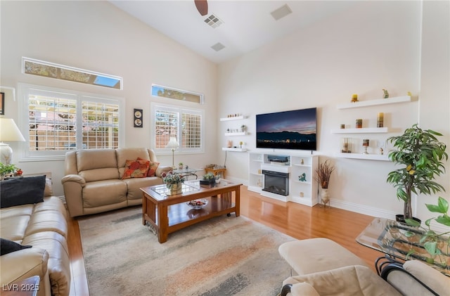 living room featuring visible vents, high vaulted ceiling, a ceiling fan, wood finished floors, and a glass covered fireplace