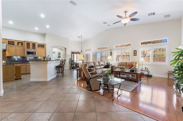 living room featuring light tile patterned floors, visible vents, high vaulted ceiling, and a ceiling fan