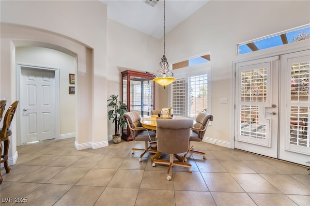 dining space featuring baseboards, arched walkways, french doors, light tile patterned flooring, and high vaulted ceiling