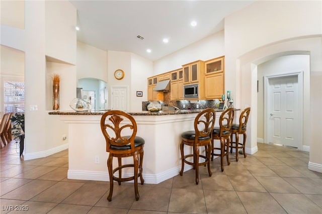 kitchen with visible vents, stainless steel microwave, a kitchen breakfast bar, tasteful backsplash, and arched walkways