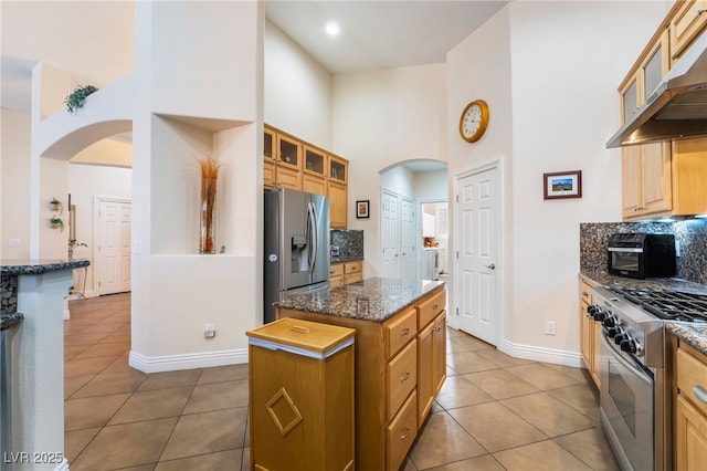 kitchen with a kitchen island, arched walkways, stainless steel appliances, under cabinet range hood, and tile patterned floors