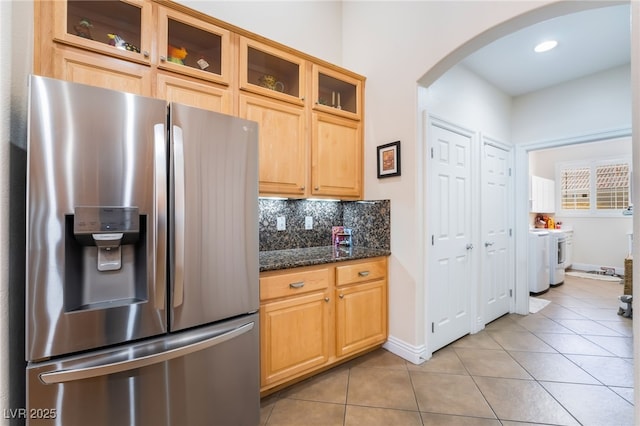 kitchen with washing machine and clothes dryer, backsplash, light tile patterned floors, stainless steel refrigerator with ice dispenser, and arched walkways