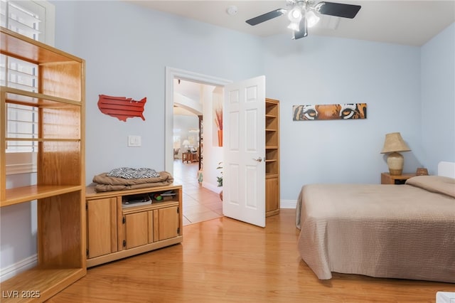 bedroom with light wood-style flooring, baseboards, arched walkways, and ceiling fan