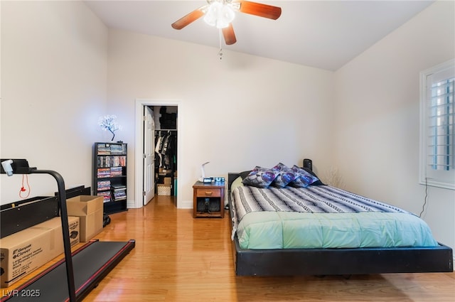 bedroom featuring a spacious closet, baseboards, ceiling fan, light wood-style floors, and a closet