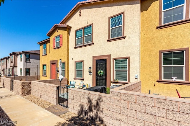 view of property featuring a tiled roof, stucco siding, and fence