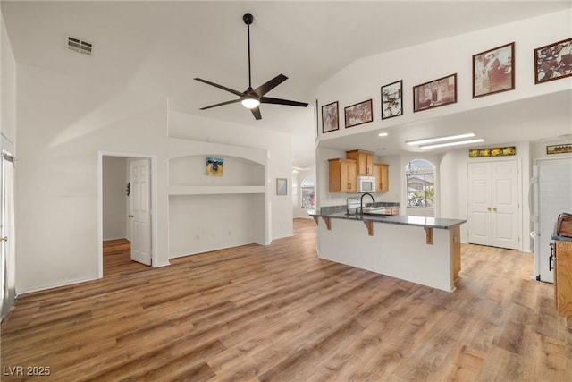 kitchen with white microwave, a peninsula, a sink, visible vents, and a kitchen breakfast bar