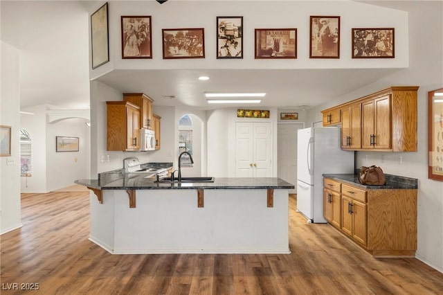 kitchen featuring arched walkways, a peninsula, white appliances, a sink, and a kitchen bar