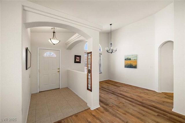 foyer entrance with light wood-style flooring, arched walkways, and a notable chandelier