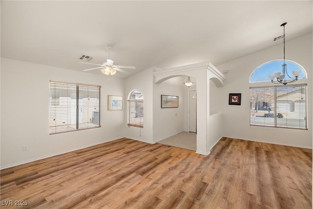 unfurnished room featuring arched walkways, vaulted ceiling, visible vents, and light wood-style floors