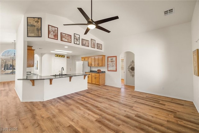 kitchen with a breakfast bar, arched walkways, visible vents, freestanding refrigerator, and a sink